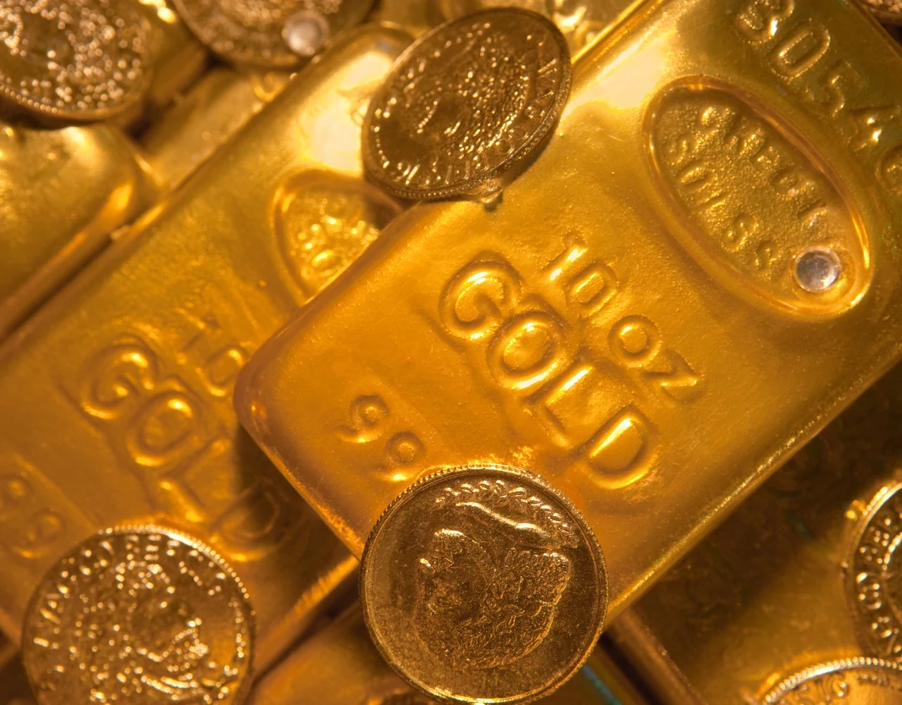 Close crop of a ten ounce gold bar stamped 999 surrounded by gold coins